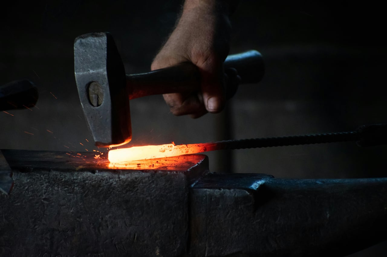 Herrero trabajando una pieza de metal caliente sobre un yunque