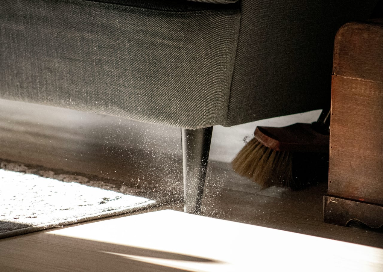 Persona barriendo polvo debajo de un sillón en una limpieza residencial
